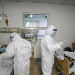 "two doctors on full body PPE attending to two patients in a covid isolation centre"