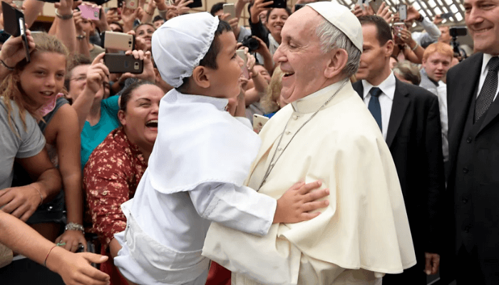 Francis lifts a child dressed like him as he greets the faithful at the end of his weekly general audience in the Paul VI Hall at the Vatican on August 23, 2017. [L'Osservatore Romano via AP]