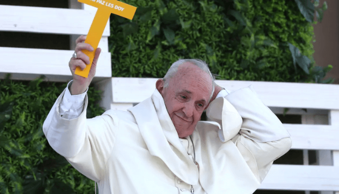 Francis loses his skull cap as he holds up a cross with Spanish words that read, "I give you my peace," upon his arrival to meet with young people at the Shrine of Maipu in Santiago, Chile, on January 17, 2018. [Alessandra Tarantino/AP Photo] 