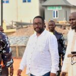 Amadu Sule in a white shirt, standing between a police officer and a man in cream kaftan
